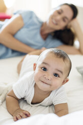 Mother looking at baby boy while lying on bed at home - CAVF39521