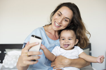 Glückliche Mutter, die ein Selfie macht, während sie mit ihrem Sohn auf dem Bett zu Hause sitzt - CAVF39523