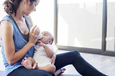 Mother feeding baby boy while sitting by window at home - CAVF39531