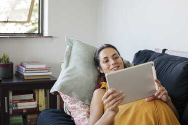 Schwangere Frau benutzt einen Tablet-Computer, während sie zu Hause auf dem Sofa liegt - CAVF39542