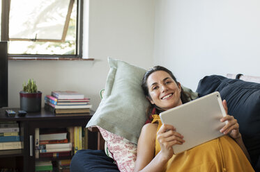 Portrait of pregnant woman using tablet computer while lying on sofa at home - CAVF39543