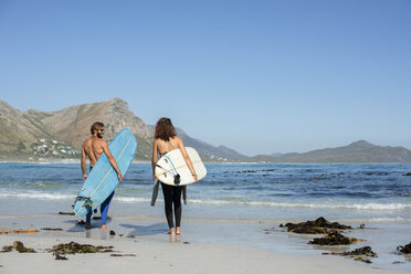 Rear view of friends carrying surfboard while walking at beach during sunny day - CAVF39555