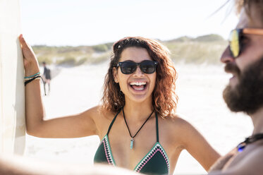 Glückliche Frau im Gespräch mit männlichem Freund am Strand an einem sonnigen Tag - CAVF39560