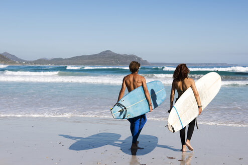 Rückansicht von Freunden mit Surfbrettern am Strand an einem sonnigen Tag - CAVF39561