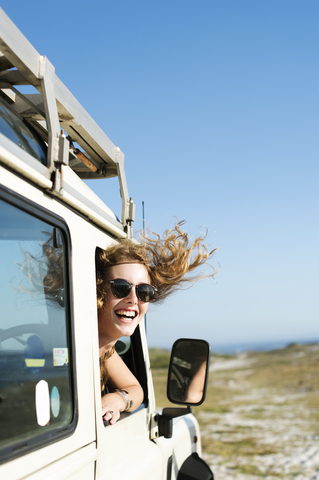 Glückliche Frau mit Sonnenbrille, die an einem sonnigen Tag durch ein Autofenster blickt, lizenzfreies Stockfoto