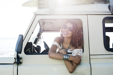 Glückliche Frau mit Sonnenbrille schaut durch ein Autofenster an einem sonnigen Tag - CAVF39573