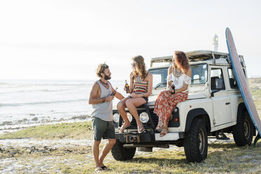 Friends holding beer bottles talking at beach against clear sky - CAVF39579