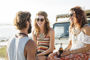 Ein Mann unterhält sich mit seinen Freundinnen und genießt ein Bier, während er auf einem Geländewagen sitzt - CAVF39581