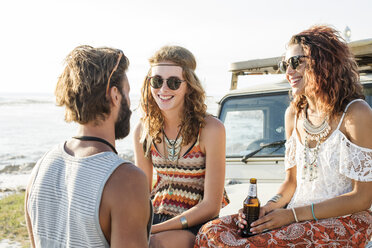 Man talking to female friends enjoying beer while sitting on off-road vehicle - CAVF39581