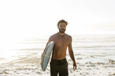 Porträt eines Mannes ohne Hemd, der ein Surfbrett trägt, während er am Strand gegen den klaren Himmel läuft - CAVF39585