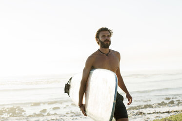 Mann ohne Hemd, der ein Surfbrett trägt, während er am Strand gegen den klaren Himmel läuft - CAVF39586
