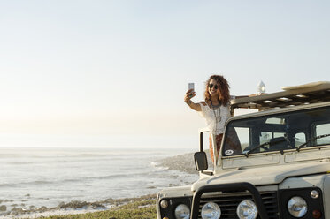 Glückliche Frau, die ein Selfie macht, während sie auf einem Geländewagen am Strand steht - CAVF39587