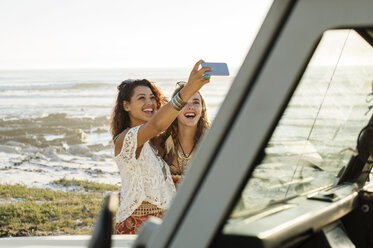 Glückliche Freundinnen, die ein Selfie machen, während sie am Strand neben einem Geländewagen stehen - CAVF39589