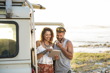 Woman showing tablet computer to boyfriend while standing by off-road vehicle at beach - CAVF39595