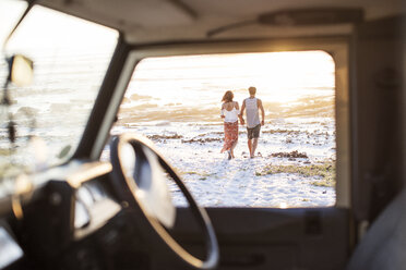 Rückansicht eines Paares, das am Strand spazieren geht, gesehen durch das Fenster eines Geländewagens - CAVF39598