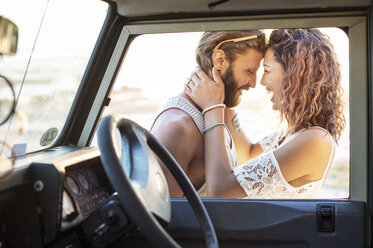Fröhliches Paar, das sich gegenseitig ansieht, während es neben einem Geländewagen steht, gesehen durch ein Fenster - CAVF39601
