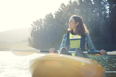 Smiling woman kayaking on lake against sky during sunny day - CAVF39627