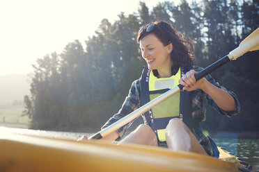 Happy woman kayaking on lake against sky during sunny day - CAVF39628