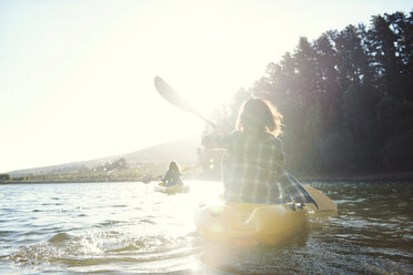 Rear view of female friends kayaking on lake during sunny day - CAVF39633