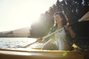 Smiling woman looking away while kayaking on lake during sunny day - CAVF39637