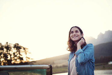 Frau schaut weg, während sie bei Sonnenuntergang neben einem Cabrio gegen den klaren Himmel steht - CAVF39652