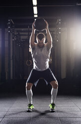 Entschlossener männlicher Sportler beim Training mit einem Medizinball im Fitnessstudio - CAVF39672