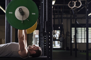 Seitenansicht eines entschlossenen männlichen Athleten, der eine Langhantel im Fitnessstudio hebt - CAVF39682