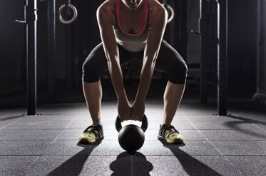 Low section of female athlete lifting kettle bell at gym - CAVF39683