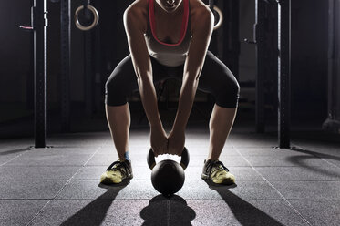 Tiefschnitt einer Sportlerin beim Heben einer Kettlebell im Fitnessstudio - CAVF39683