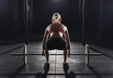 Rückansicht einer Frau, die eine Langhantel im Fitnessstudio aufnimmt - CAVF39689