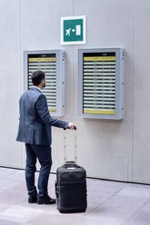 Rückansicht eines Geschäftsmannes, der mit seinem Gepäck in einer U-Bahn-Station steht und die Ankunfts- und Abfahrtstafel liest - CAVF39705