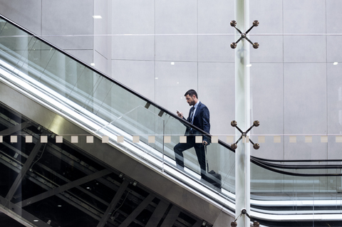 Geschäftsmann benutzt Smartphone auf Rolltreppe in U-Bahn-Station, lizenzfreies Stockfoto