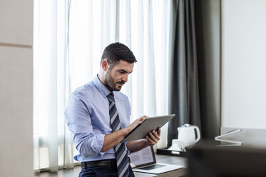 Businessman using tablet computer while standing by window in hotel room - CAVF39734