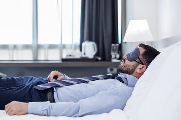 Side view of businessman wearing eye mask while sleeping in hotel room - CAVF39744