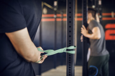 Midsection of man holding resistance band tied to pole in gym - CAVF39756