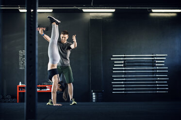 Fitness-Lehrer, der einer Frau beim Handstand im Fitnessstudio hilft - CAVF39762