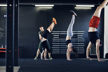 Trainer, der einem Sportler beim Handstand im Fitnessstudio hilft - CAVF39763