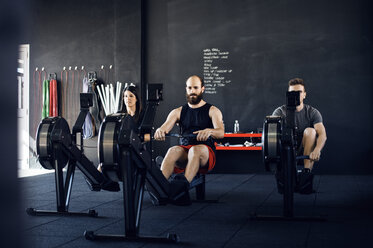 Entschlossene Athleten trainieren auf einem Rudergerät im Fitnessstudio - CAVF39765