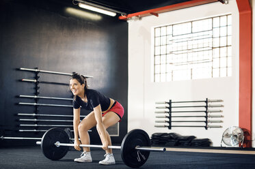 Happy woman lifting barbell in gym - CAVF39779