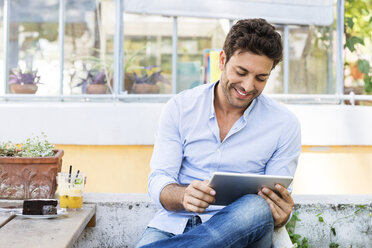 Lächelnder Mann, der einen Tablet-Computer benutzt, während er in einem Straßencafé sitzt - CAVF39797