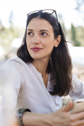 Thoughtful woman holding smart phone while sitting at sidewalk cafe - CAVF39801