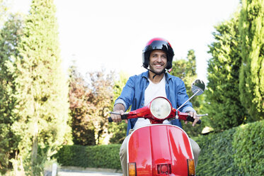 Glücklicher Mann fährt Motorroller inmitten von Bäumen - CAVF39809