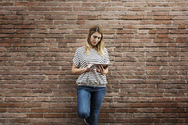 Woman using tablet computer while standing against brick wall - CAVF39858