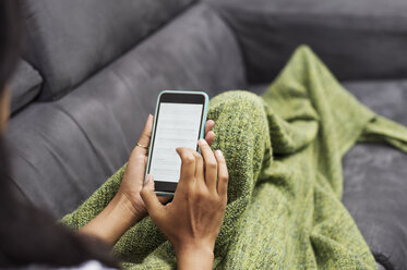 Cropped image of woman using phone while lying on sofa at home - CAVF39880