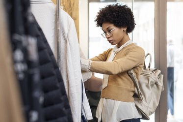 Konzentrierte Frau auf der Suche nach Oberteilen an einem Kleiderständer in einem Geschäft - CAVF39881