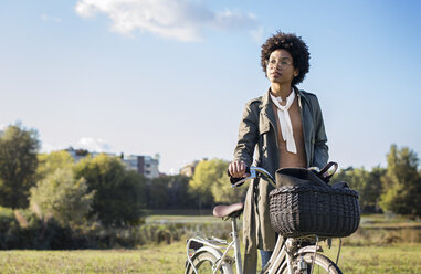 Nachdenkliche Frau mit Fahrrad auf einem Feld gegen den klaren Himmel stehend - CAVF39887