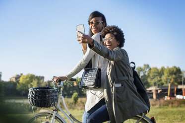 Glückliche Freunde nehmen Selfie durch Telefon beim Fahrradfahren auf Feld - CAVF39888