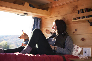 Woman relaxing on bed in camper van - CAVF39923