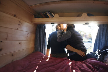 Rückansicht eines Paares, das sich küsst, während es auf dem Bett eines Wohnmobils sitzt - CAVF39925