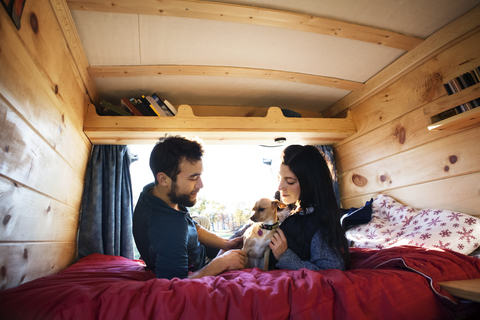 Ehepaar betrachtet den Hund, während es sich auf dem Bett im Wohnmobil entspannt, lizenzfreies Stockfoto